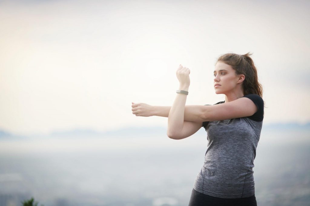 Young woman stretching outdoors in a calm environment, representing physical movement, focus, and body awareness.