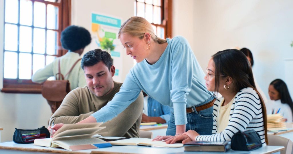 Teacher guiding students in a classroom while reviewing a book together, showing support, collaboration, and active learning.