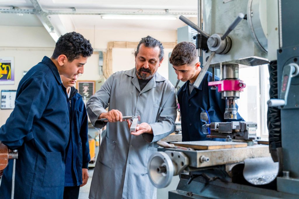 Instructor guiding students in a workshop using machinery, demonstrating hands-on learning and practical skill development.