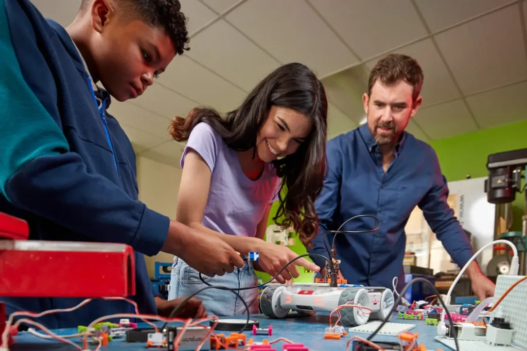 Students working together on a robotics project with a teacher in a hands-on STEM classroom environment.