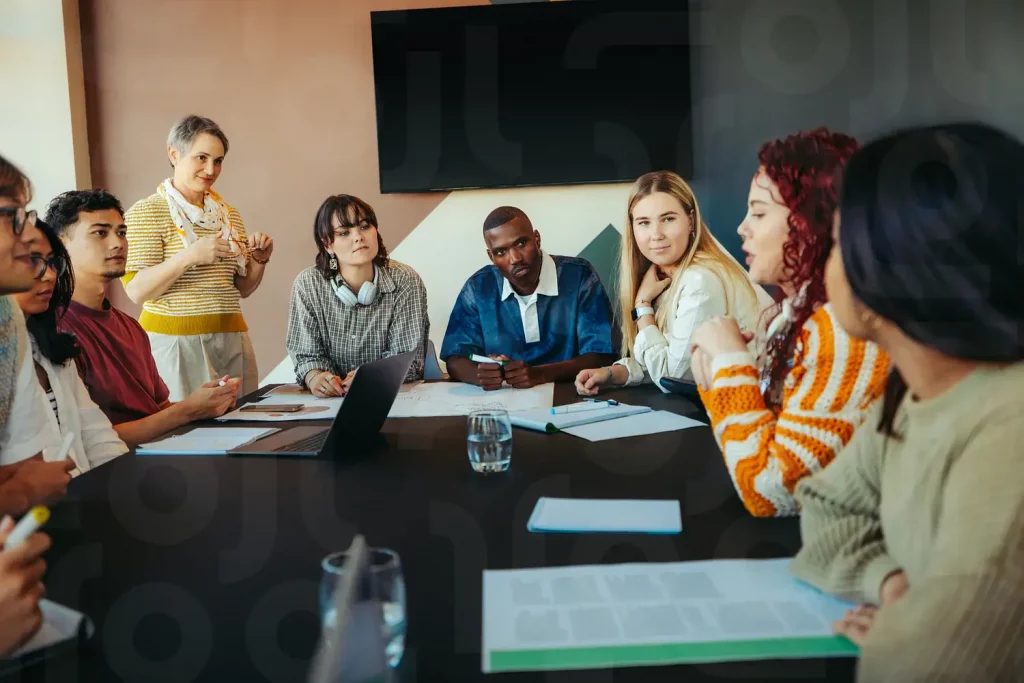Group of students and a teacher discussing ideas around a table in a collaborative classroom environment.