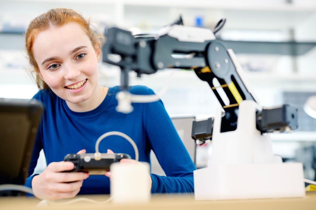 Young person controlling a robotic arm in a lab setting, demonstrating hands-on learning, technology engagement, and skill development.