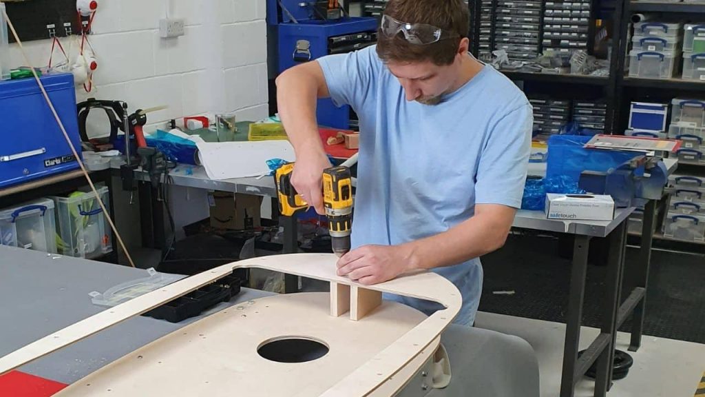 Person using a power drill to assemble a wooden structure in a workshop, demonstrating hands-on building and practical skills.
