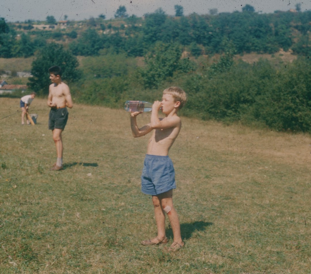 Child drinking from a water bottle in a grassy outdoor area