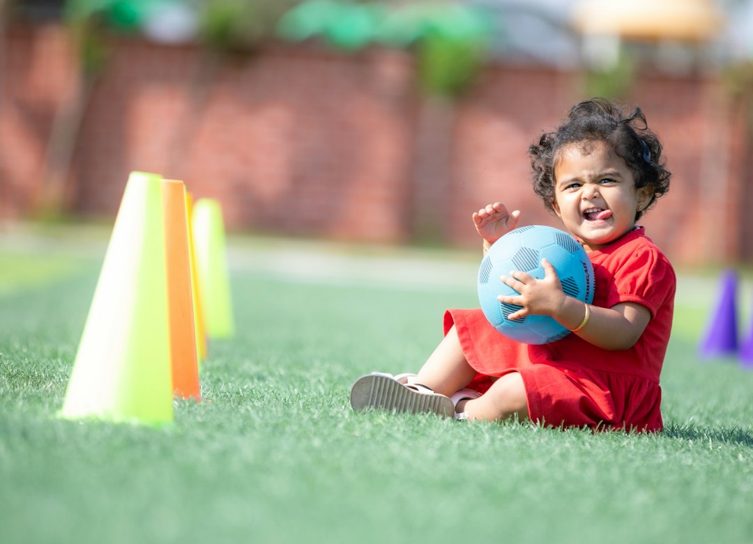 Young child sitting on the ground beside a ball