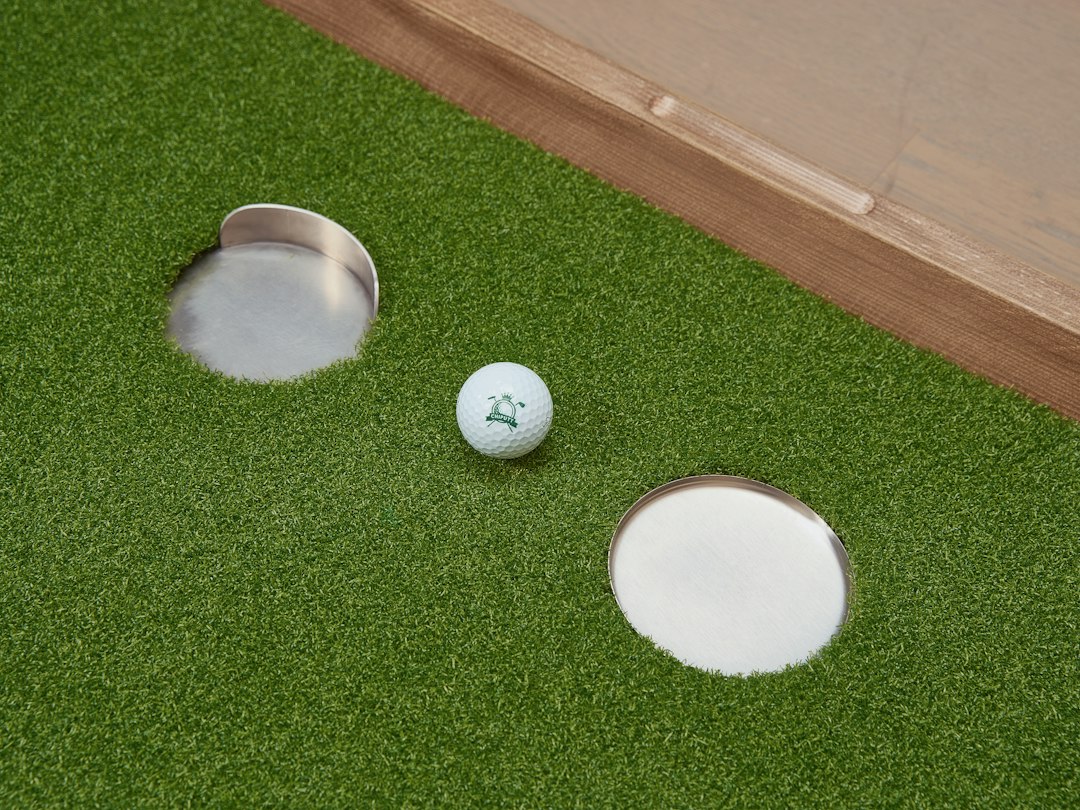 Golf ball beside two circular targets on a green indoor putting surface